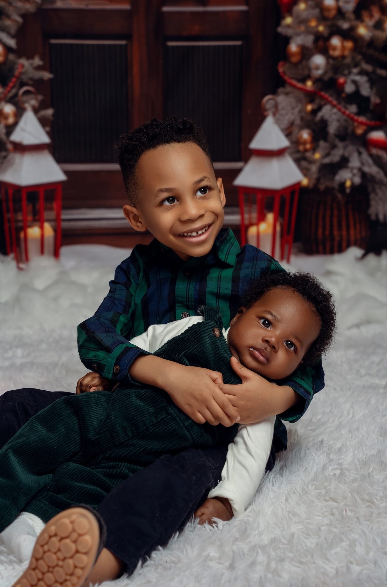 Brothers hugging on the floor beside a decorated Christmas tree