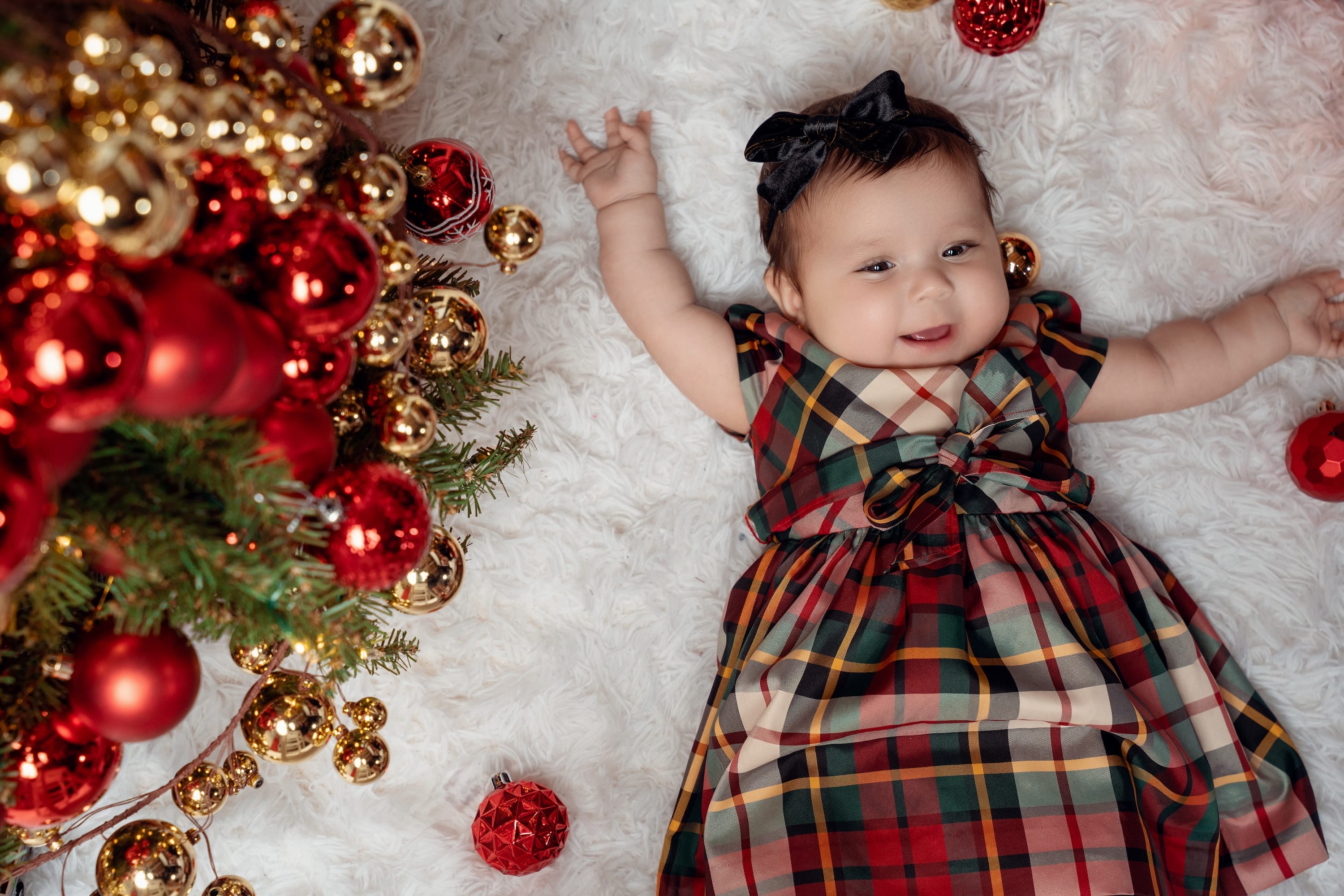 Smiling girl in a plaid dress beside a decorated Christmas tree