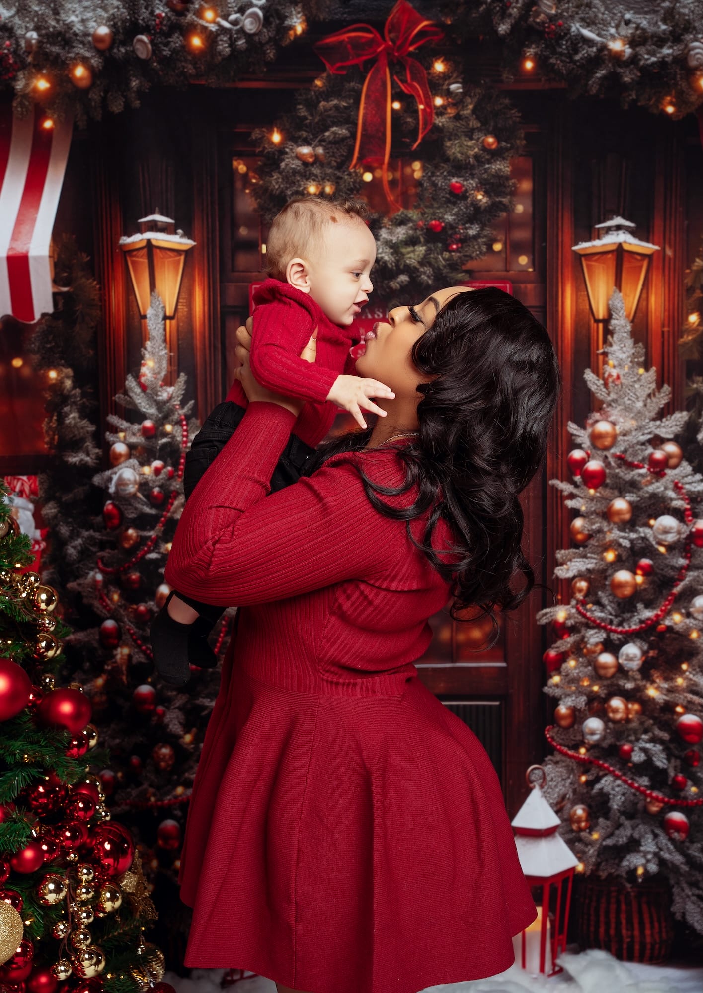 Mother kissing her baby beside a decorated Christmas tree