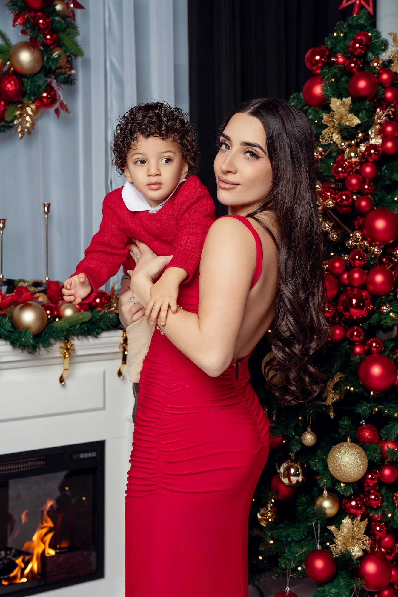Mother and son posing by a glowing fireplace in a Christmas photo studio