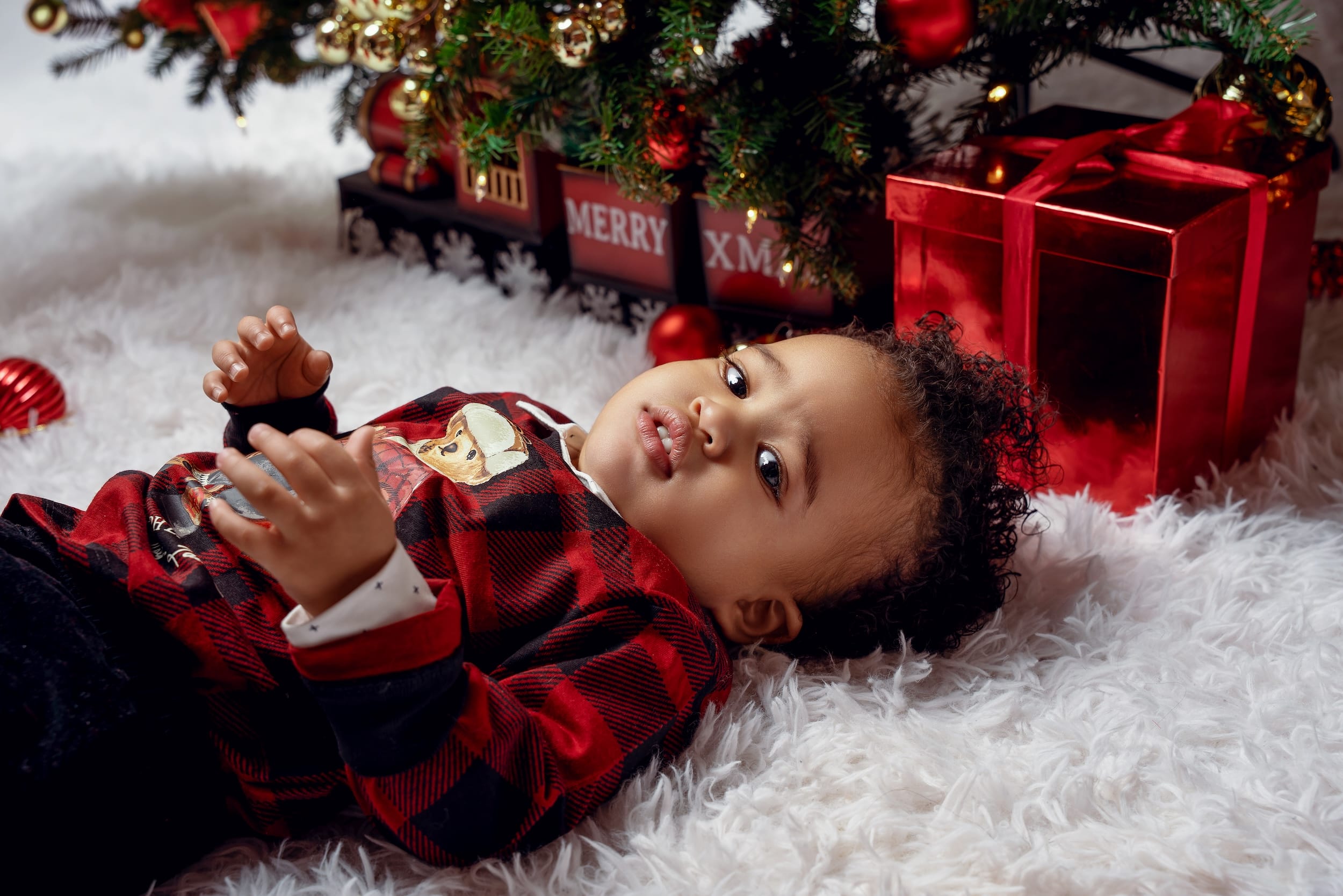 Baby boy lying under a Christmas tree surrounded by gifts