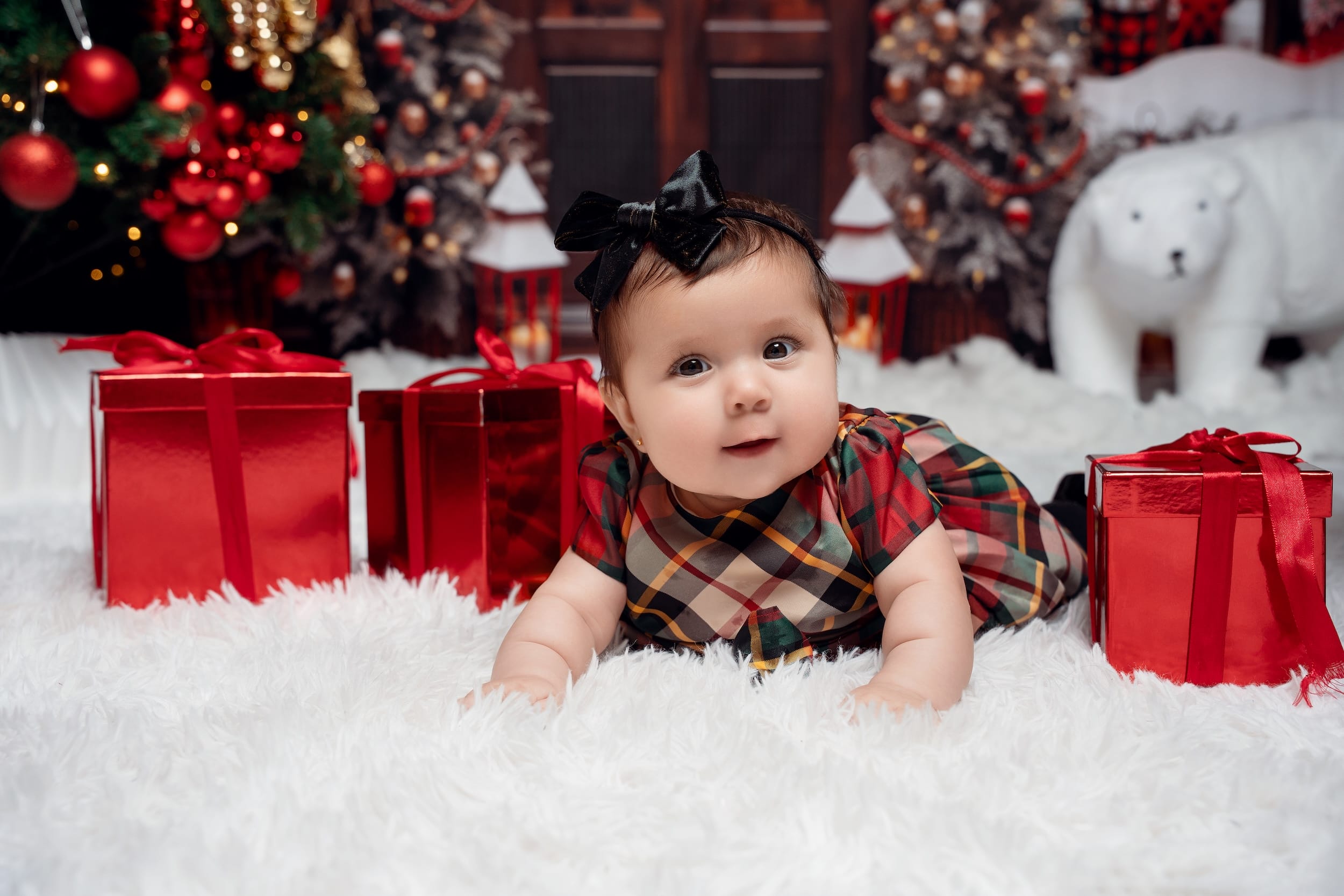 Baby girl in a plaid dress lying among red Christmas gifts